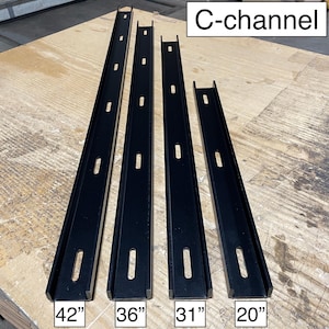 May include: Four black C-channel metal pieces of varying lengths: 42", 36", 31", and 20". Each channel has evenly spaced rectangular cutouts. The text "C-channel" is in a white box in the upper right corner. The pieces are on a light brown wooden surface.