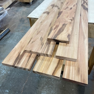 May include: Four pieces of wood with a natural wood grain pattern. The wood is light brown with dark brown streaks. The wood is stacked on top of each other.