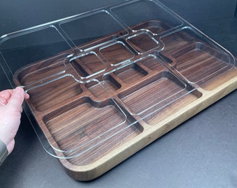 May include: A wooden tray with a clear acrylic lid. The tray has multiple compartments of different sizes. The lid is slightly lifted to show the compartments.