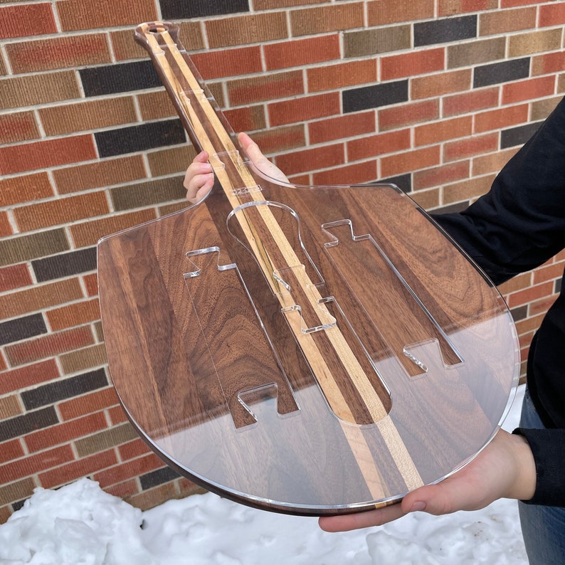May include: A clear acrylic pizza cutter with a walnut wood base. The cutter has a unique design with multiple slots for cutting pizza slices.
