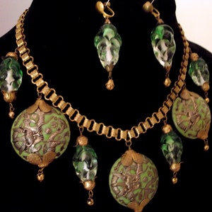 May include: A gold chain necklace with green and white glass beads and a pendant with a green and gold design. The necklace is paired with matching earrings.