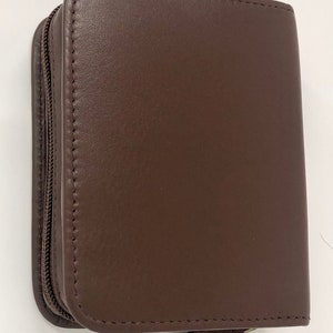May include: A brown leather zipped case with a zipper pull. The case is closed.
