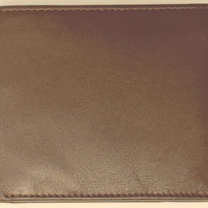 May include: A bifold wallet crafted from smooth, dark brown leather. The exterior features a clean, rectangular design with visible tonal stitching along the edges, providing a structured and uniform appearance for this classic everyday accessory.
