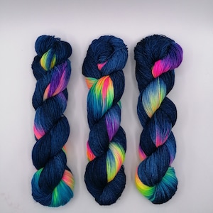 Puede incluir: Tres ovillos de hilo de color azul oscuro con un arcoíris de colores tejidos.