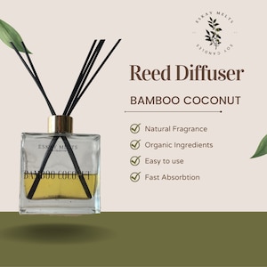 May include: A clear glass reed diffuser bottle with a gold lid and black reeds. The bottle is filled with a light brown liquid and has a label that reads "ESKAY MELTS COLLECTION BAMBOO COCONUT REED DIFFUSER". The background is a light brown color with green leaves.