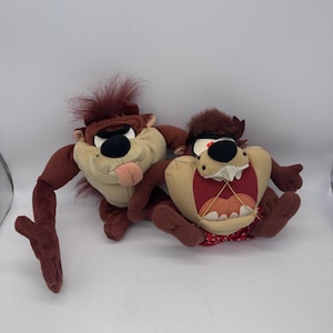 May include: Two plush Tazmanian Devil stuffed animals. One is standing with its tongue out, and the other is sitting with its mouth open. Both have brown fur, black noses, and red accents.