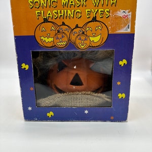 May include: A cardboard box with a blue background and stars. The box features a window showing a pumpkin mask with flashing eyes. The text on the box reads "Sonic Mask with Flashing Eyes".