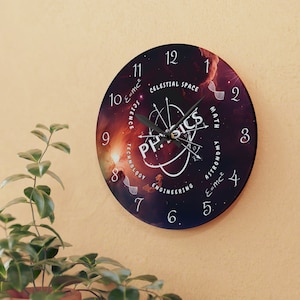 Op de afbeelding: Een ronde klok met een zwarte achtergrond en een nevelachtig ontwerp. De wijzerplaat van de klok heeft het woord "PHYSICS" in een witte cirkel met een gestileerd atoomsymbool. De cijfers 1 tot en met 12 worden weergegeven rond de rand van de wijzerplaat, met de woorden "CELESTIAL SPACE", "SCIENCE", "TECHNOLOGY", "ENGINEERING", "MATH", "ASTRONOMY" en "E=mc²" rond het atoomsymbool geschreven.