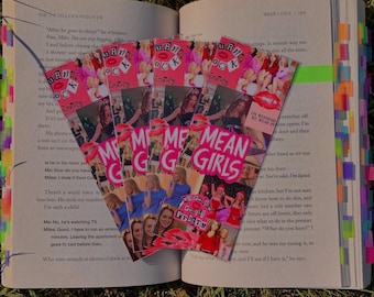 May include: A set of five pink and white bookmarks featuring images from the movie Mean Girls. The bookmarks have the text "Mean Girls" and "You Can't Sit With Us" on them.