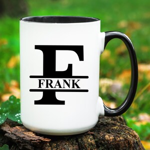 May include: White ceramic mug with a black handle and a black rim. The mug has a black letter "F" with the name "FRANK" printed in black below the letter.