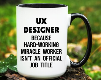 May include: White ceramic mug with a black interior and handle. The mug features the text "UX DESIGNER BECAUSE HARD-WORKING MIRACLE WORKER ISN'T AN OFFICIAL JOB TITLE" in bold black letters.