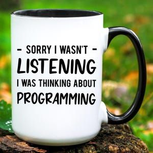 May include: White coffee mug with a black rim and handle. The mug has black text that reads "Sorry I wasn't listening I was thinking about programming."
