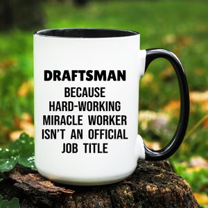 May include: White ceramic mug with a black interior and handle. The mug features the text "DRAFTSMAN BECAUSE HARD-WORKING MIRACLE WORKER ISN'T AN OFFICIAL JOB TITLE" in bold black letters.