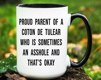 May include: White ceramic mug with a black interior and handle. The mug features the text "PROUD PARENT OF A COTON DE TULEAR WHO IS SOMETIMES AN ASSHOLE AND THAT'S OKAY" in black, centered on the front.