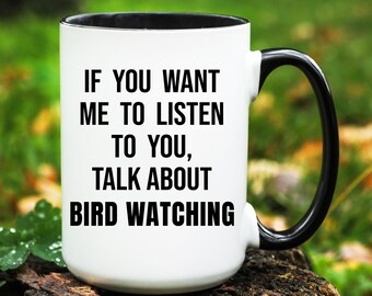 May include: White ceramic mug with a black interior and handle. The mug features the text: "IF YOU WANT ME TO LISTEN TO YOU, TALK ABOUT BIRD WATCHING" in black, bold font. The mug is sitting on a wooden surface.