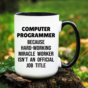May include: White ceramic mug with a black interior and handle. The mug features the text "COMPUTER PROGRAMMER BECAUSE HARD-WORKING MIRACLE WORKER ISN'T AN OFFICIAL JOB TITLE" in black, bold font.
