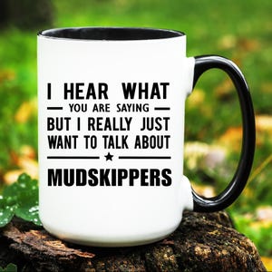 May include: White ceramic mug with a black handle and rim. The mug features the text "I HEAR WHAT YOU ARE SAYING BUT I REALLY JUST WANT TO TALK ABOUT MUDSKIPPERS" in black, with a star graphic.