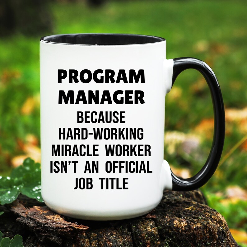 May include: White ceramic mug with a black interior and handle. The mug features the text "PROGRAM MANAGER BECAUSE HARD-WORKING MIRACLE WORKER ISN'T AN OFFICIAL JOB TITLE" in bold black letters.