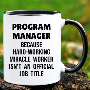 May include: A white ceramic mug with a black interior and handle. The mug features the text "PROGRAM MANAGER BECAUSE HARD-WORKING MIRACLE WORKER ISN'T AN OFFICIAL JOB TITLE" in bold black letters.