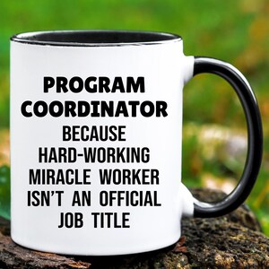 May include: White ceramic mug with a black interior and handle. The mug features the text "PROGRAM COORDINATOR BECAUSE HARD-WORKING MIRACLE WORKER ISN'T AN OFFICIAL JOB TITLE" in black, bold font.