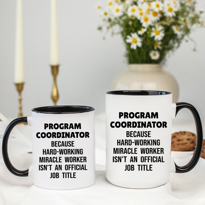 May include: Two white ceramic mugs with black handles and rims. The mugs have the text "PROGRAM COORDINATOR BECAUSE HARD-WORKING MIRACLE WORKER ISN'T AN OFFICIAL JOB TITLE" in black. One mug is smaller than the other.