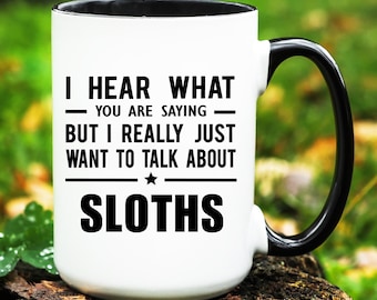 May include: White ceramic mug with a black interior, handle, and rim. The mug features the text "I HEAR WHAT YOU ARE SAYING BUT I REALLY JUST WANT TO TALK ABOUT SLOTHS" in black, centered on the front.