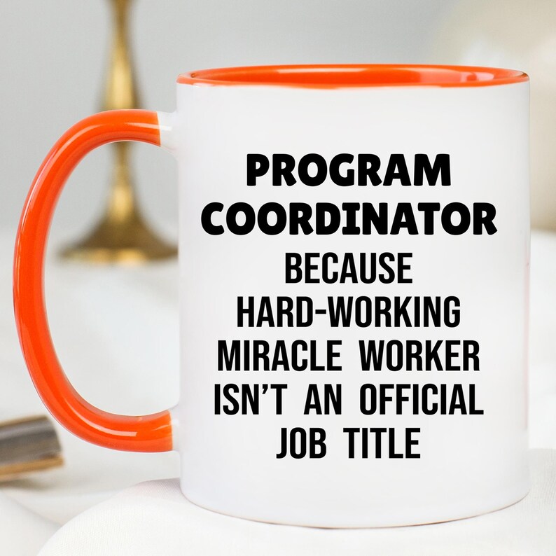 May include: White ceramic mug with an orange handle and rim. The mug features the text "PROGRAM COORDINATOR BECAUSE HARD-WORKING MIRACLE WORKER ISN'T AN OFFICIAL JOB TITLE" in black, bold font.