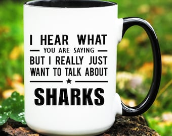 May include: White ceramic mug with a black handle and rim. The mug features the text "I HEAR WHAT - YOU ARE SAYING - BUT I REALLY JUST WANT TO TALK ABOUT SHARKS" in black, with a star graphic.
