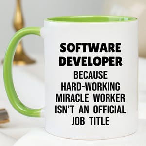 May include: White ceramic mug with a green handle and interior. The mug features the text "SOFTWARE DEVELOPER BECAUSE HARD-WORKING MIRACLE WORKER ISN'T AN OFFICIAL JOB TITLE" in black, bold letters.
