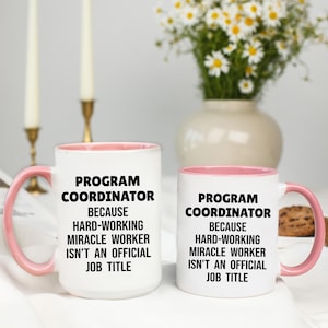May include: Two white ceramic mugs with pink interiors and handles. The mugs have the text "PROGRAM COORDINATOR BECAUSE HARD-WORKING MIRACLE WORKER ISN'T AN OFFICIAL JOB TITLE" in black.