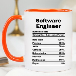 May include: White ceramic mug with an orange handle and rim. The mug features the text "Software Engineer" and a "Nutrition Facts" label with percentages for hard work, passion, skills, caffeine, determination, patience, multitasking, and regret.