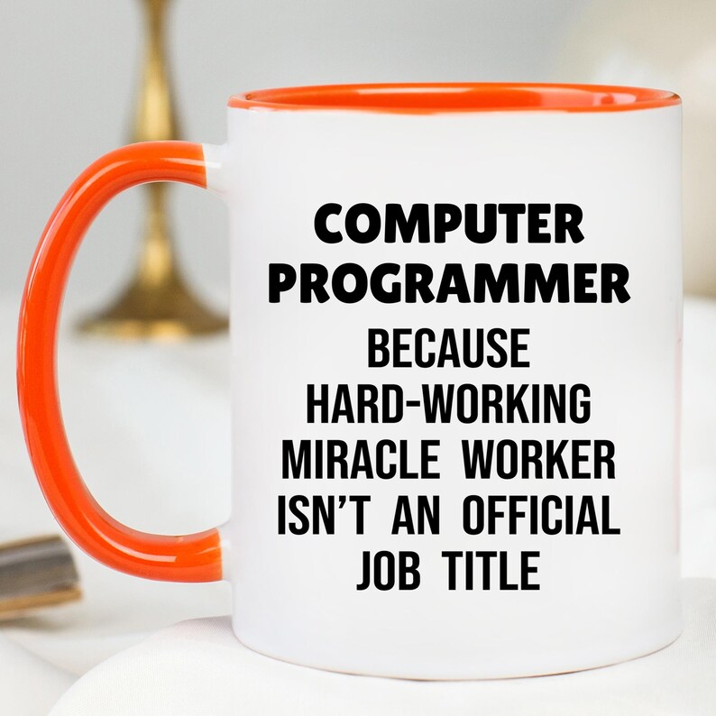 May include: White ceramic mug with an orange handle and rim. The mug features the text "COMPUTER PROGRAMMER BECAUSE HARD-WORKING MIRACLE WORKER ISN'T AN OFFICIAL JOB TITLE" in bold black letters. A humorous gift for programmers.
