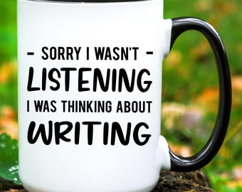 May include: White ceramic coffee mug with a black handle and black rim. The mug has black text that reads "Sorry I wasn't listening I was thinking about writing."