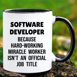 May include: White ceramic mug with a black rim and handle. The mug features the text "SOFTWARE DEVELOPER BECAUSE HARD-WORKING MIRACLE WORKER ISN'T AN OFFICIAL JOB TITLE" in bold black letters.