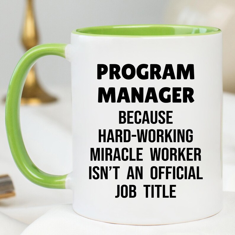 May include: White ceramic mug with a green handle and interior. The mug features the text "PROGRAM MANAGER BECAUSE HARD-WORKING MIRACLE WORKER ISN'T AN OFFICIAL JOB TITLE" in bold black letters.