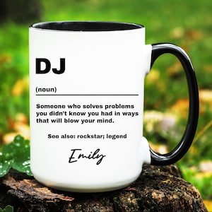 May include: White ceramic mug with a black handle and rim. The mug features the word "DJ" in bold black letters, followed by a definition. The text reads "Someone who solves problems you didn't know you had in ways that will blow your mind." The name "Emily" is written in cursive.