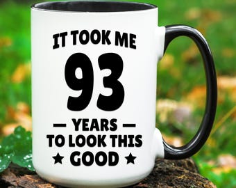 May include: White coffee mug with a black handle and black interior. The mug has black text that reads "It took me 93 years to look this good." with a star on either side of the word "good".