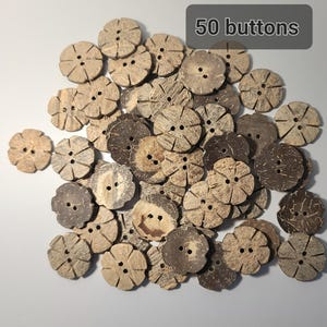 May include: A collection of 50 flower-shaped buttons made from natural coconut shells. The buttons are various shades of brown and tan, with two or four holes for sewing. The text "50 buttons" is in a gray rectangle.
