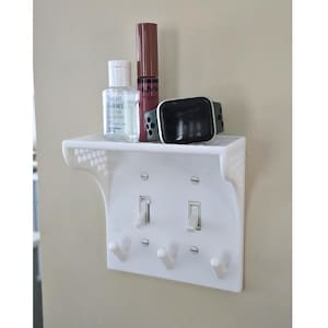 Könnte beinhalten: Ein weißes Plastikregal mit Haken und zwei Lichtschaltern. Das Regal ist über einer Lichtschalterplatte montiert. Auf dem Regal befinden sich drei Gegenstände: eine kleine Flasche Handdesinfektionsmittel, eine Tube Lippenstift und eine Smartwatch.