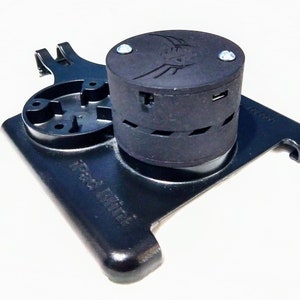 Puede incluir: Soporte negro para iPad Mini con un componente cilíndrico negro con un logotipo y dos tornillos. El soporte tiene una base rectangular con bordes redondeados y el texto "iPad Mini" impreso. El soporte tiene un componente circular con agujeros.