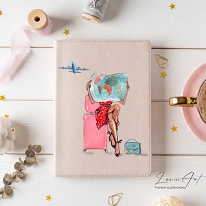 Pu&ograve; includere: Un diario di viaggio rosa con un motivo a pois bianchi. La copertina presenta una donna seduta su una valigia rosa che tiene una mappa del mondo. Il testo "Let's Travel" &egrave; sulla valigia. Il diario &egrave; su una superficie di legno bianco con stelle dorate e una tazza di caff&egrave;.