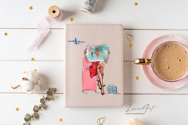 Pu&ograve; includere: Un diario di viaggio rosa con un motivo a pois bianchi. La copertina presenta una donna seduta su una valigia rosa che tiene una mappa del mondo. Il testo "Let's Travel" &egrave; sulla valigia. Il diario &egrave; su una superficie di legno bianco con stelle dorate e una tazza di caff&egrave;.