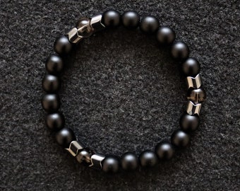 May include: A black beaded bracelet with silver accents. The bracelet is made of round black beads and silver metal accents.