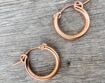 Könnte beinhalten: Ein Paar Ohrringe aus roségold. Die Ohrringe sind klein und schlicht, mit einer glatten Oberfläche.