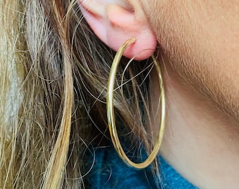 Pode incluir: Um par de brincos de argola de ouro usados na orelha de uma pessoa.
