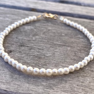 Puede incluir: Un brazalete de perlas blancas con un cierre dorado.