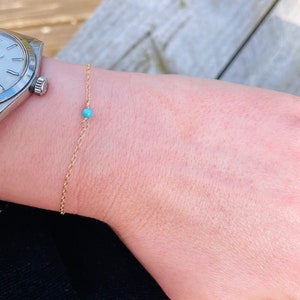 Puede incluir: Un delicado brazalete de cadena dorada con una sola cuenta turquesa.