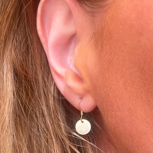 May include: A pair of gold-toned earrings with a small, round disc pendant. The earrings are simple and delicate, perfect for everyday wear.