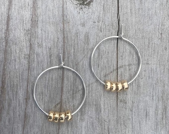 May include: A pair of silver hoop earrings with gold beads. Each earring has five gold beads.