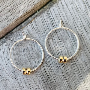 Op de afbeelding: Een paar zilveren creolen met een klein gouden kraalaccent op elke creool.